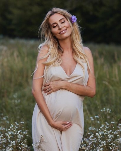 36-latka wstawiła na Instagram zdjęcie, do których pozuje w beżowej sukience na tle łąki i trzyma się za brzuszek ciążowy, który jest już całkiem spory.