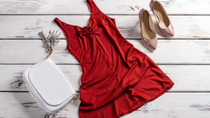Na podłodze leży sukienka z dekoltem kopertowym w kolorze czerwonym, szpilki i biała torebka