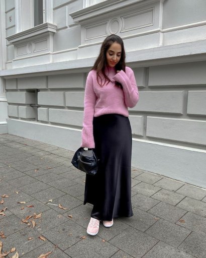 Ciepły sweterek w pastelowym różu, długa czarna i atłasowa spódnica, mini czarna torebka plus sportowe buty w kolorze sweterka.